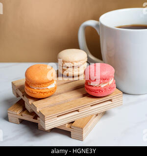 Macarons colorés et sucrés servis sur de petites palettes bois avec tasse de café sur une texture de marbre table et fond doré. Dessert traditionnel français. Copier l'espace. Banque D'Images