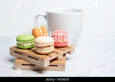 Macarons colorés et sucrés servis sur de petites palettes bois avec tasse de café sur une texture en arrière-plan. Dessert traditionnel français. Banque D'Images