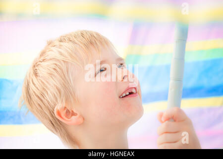 Cute child boy à l'âge scolaire avec des dents de lait manquantes sous sourire parapluie parasol de couleur pastel Banque D'Images