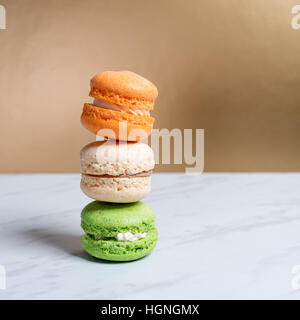 Macarons colorés et doux empilés sur une texture de marbre table et fond doré. Dessert traditionnel français. Copier l'espace. Banque D'Images