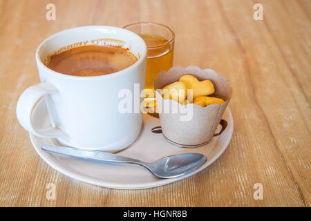 Tasse de café en blanc sur le disque avec de petits cookies sur table en bois, la lumière de la fenêtre Banque D'Images