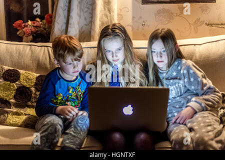 Les enfants assis à la maison à la recherche d'un ordinateur à rire à une émission de télévision Banque D'Images