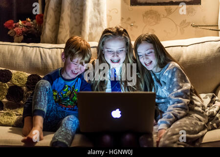 Les enfants assis à la maison à la recherche d'un ordinateur à rire à une émission de télévision Banque D'Images