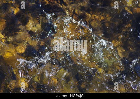 Déménagement transparente aux projections d'eau et vagues sur cuivre brown rocks dans un flux avec la lumière du soleil Banque D'Images