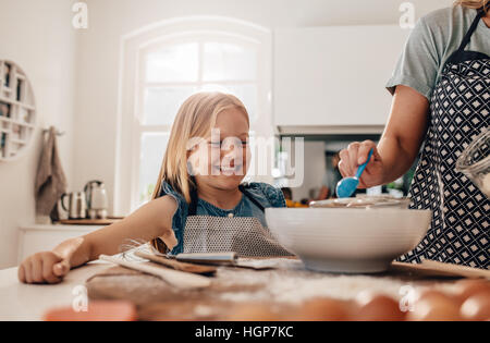 Happy little Girl standing in cuisine et sa mère à la cuisson des aliments. Mère et fille heureuse la cuisson dans la cuisine. Banque D'Images