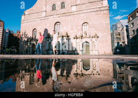 Riga, Lettonie - 1 juillet 2016 : Vue de dessous de deux jeunes hommes marchant sur la rue pavée près de Eglise Saint-Pierre et leur reflet dans la flaque après Rai Banque D'Images