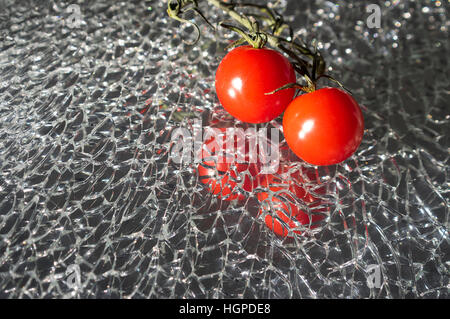 Tomates cerises fraîches mûres sur verre miroir cassé Banque D'Images