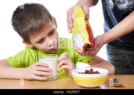 Maman prépare un chocolat Boules de maïs dans le lait pour le petit-déjeuner pour un petit garçon blanc isolé Banque D'Images