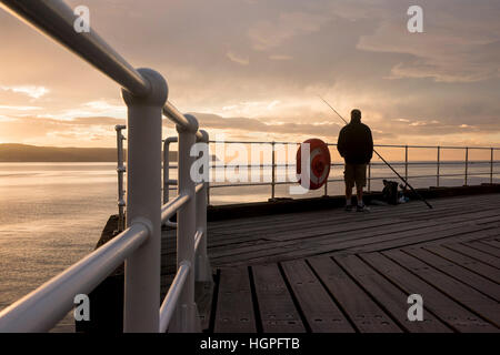 Scenic Whitby & silhouetté contre dramatique, bright colorful sunset sky, man (pêcheur) est la pêche en mer à partir de la jetée Ouest - North Yorkshire, England, UK. Banque D'Images