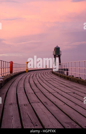 Afficher le long de la jetée Ouest Extension Whitby, North Yorkshire, Angleterre - planches en bois sous un ciel rouge, rose spectaculaire au coucher du soleil. Banque D'Images