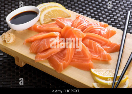 Saumon Sashimi avec du citron et de la sauce soja servi sur planche de bois, la cuisine japonaise Banque D'Images