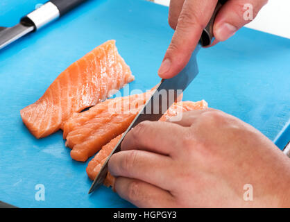 Chef slicing raw filet de saumon frais avec un couteau bien aiguisé dans un bar à sushi japonais , Vue en gros plan sur ses mains et le poisson sur une planche à découper bleu Banque D'Images