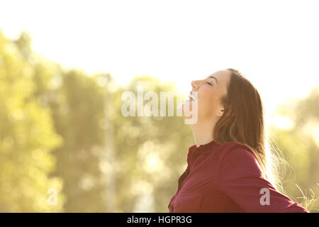 Vue latérale d'une femme heureuse de respirer l'air frais extérieur avec un fond vert et une lumière chaude Banque D'Images