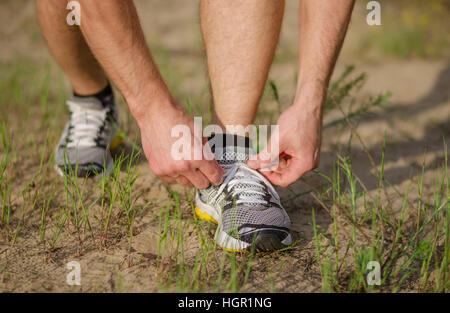 Close-up mains d'un jeune homme qui attache les lacets de chaussures d'athlétisme lors de l'exécution à l'extérieur sur une piste sablonneuse. Banque D'Images