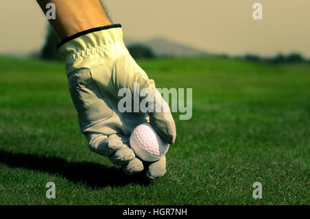 La main avec un gant est de placer une balle de golf sur le terrain. Banque D'Images