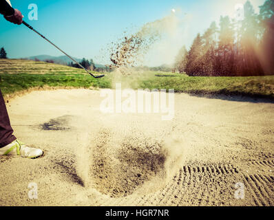 Frapper golfeur à partir d'une fosse de sable. Le golf est sur le sable. Faire des projections de sable. Soleil et soleil dans l'arrière-plan Banque D'Images