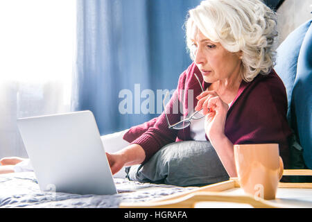 Attractive senior woman using laptop while lying on bed Banque D'Images