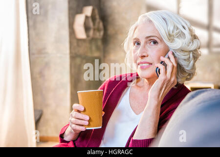 Portrait of senior Woman talking on mobile phone et tenant une tasse de boisson chaude Banque D'Images