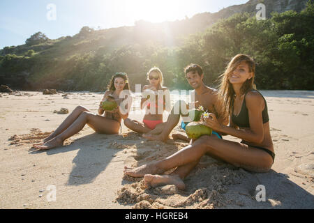 Portrait de jeune homme et femmes de boire l'eau de coco fraîche sur la plage. Groupe de jeunes amis appréciant les vacances d'été sur la plage. Banque D'Images