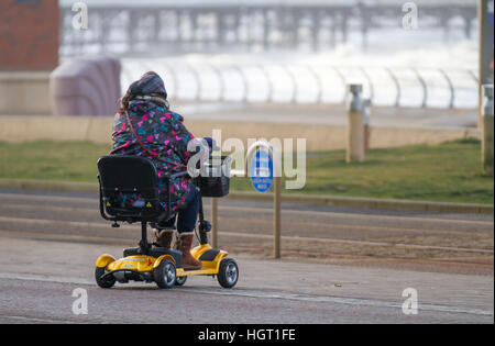 Blackpool, Lancashire, Royaume-Uni. 13 Jan 2017. Météo britannique. Senior, utilisateur de fauteuil roulant, un retraité personne handicapée à l'aide d'un scooter de mobilité. Hardy souls braver les vagues de tempête sur le célèbre Golden Mile de Blackpool front de mer. Fortes rafales ont causé d'énormes vagues de s'écraser contre les défenses de la mer. Credit : MediaWorld Images/Alamy Live News Banque D'Images