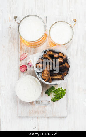 Snack-bière ensemble. Deux chopes de bière Pilsener, croûtons de pain de seigle, crème d'ail sauce au fromage et aux herbes fraîches plus backgroundwith ancienne en bois laqué blanc Banque D'Images