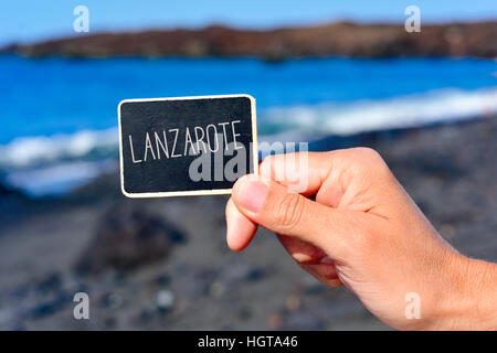Libre de la main d'un jeune homme tenant une pancarte noire avec le texte écrit en Lanzarote, dans une plage de sable noir à Lanzarote, Îles Canaries Banque D'Images