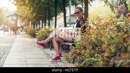 Young woman relaxing on ville banc avec son portable Banque D'Images