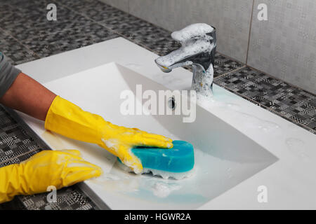 Mains de femme dans les gants qui lave dans la salle de bains lavabo blanc Banque D'Images