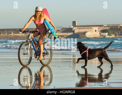 Woman riding sur son vélo avec son chien le long de la plage. Tarifa, Costa de la Luz, Cadix, Andalousie, Espagne du Sud. Banque D'Images