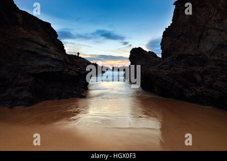 Falaises de roche entourant plage naturelle avec des vagues au coucher du soleil Banque D'Images