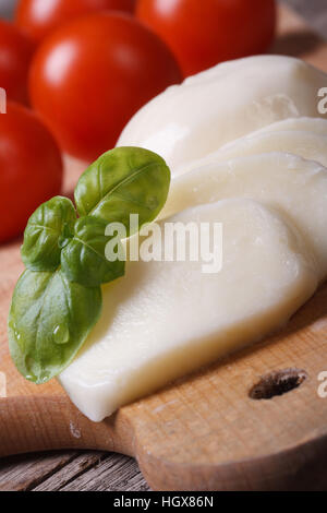 Tranches de mozzarella et de macro basilic vert sur un fond de tomates cerises rouges verticales. Banque D'Images