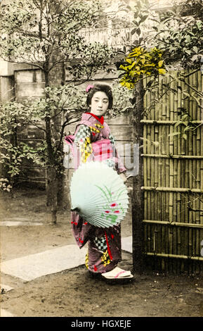 Le Japon, Vintage postcard retouchées à la main. Date de clôture en bambou par Geisha holding umbrella, habillés en kimono. Eye-contact. Vers 1910 Banque D'Images