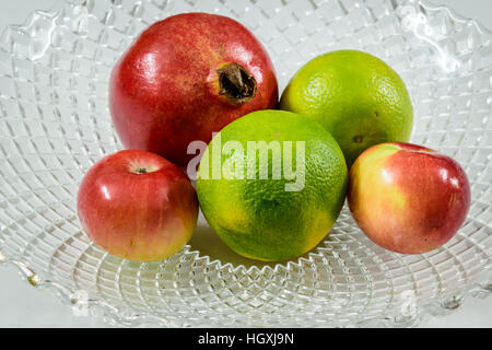 Fruits mélangés. rouge grenade limette Apple dans un bol en verre avec fond blanc. Banque D'Images