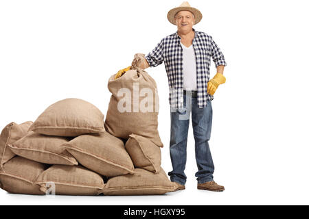 Full Length portrait of a young farmer debout à côté d'une pile de sacs de toile isolé sur fond blanc Banque D'Images