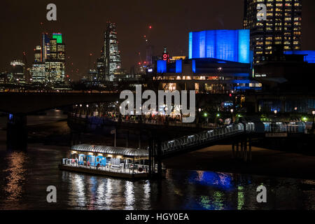 Le Théâtre National s'illumine en bleu en raison d'sponsoship Travelex. Il se reflète dans la rivière Thameswith la ville et l'Oxo tower en arrière-plan. Banque D'Images