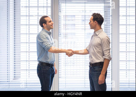 Deux collègues habillés de désinvolture shaking hands in a modern office interior comme un symbole d'accord Banque D'Images