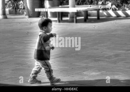 Un bambin asiatique chasing bubbles en dehors de l'entrée de la fenêtre du monde à Shenzhen, Chine. Banque D'Images