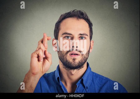 Jeune homme faisant un passage souhaite ses doigts isolé sur fond de mur gris Banque D'Images