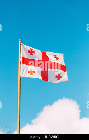 Fermer le drapeau de la Géorgie, cinq, agitant le drapeau sur mât au fond de ciel bleu ensoleillé. L'homme blanc et le symbole national, l'état civil et l'Etoile Banque D'Images