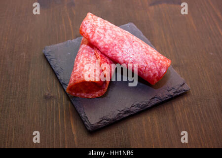 Tranches de salami sur ardoise plaque sur une table en bois Banque D'Images