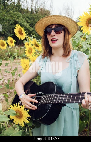 Jeune femme jouant de la guitare dans un champ de tournesols Banque D'Images