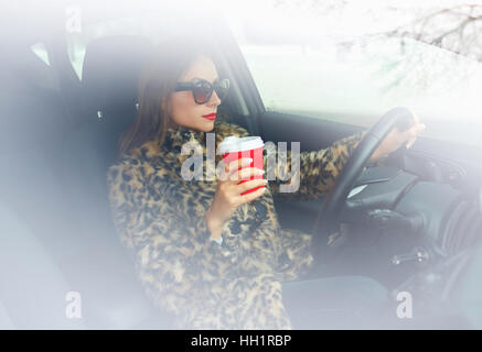 Belle femme dans un manteau de fourrure avec lèvres rouges avec du café pour aller conduire sa voiture Banque D'Images
