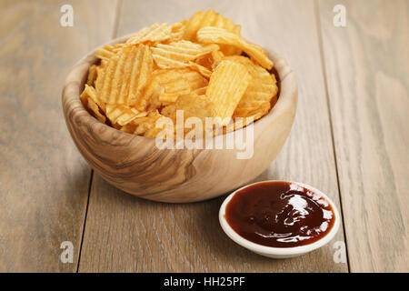 Chips de pomme de terre ridée avec le paprika et la sauce barbecue dans le bol en bois Banque D'Images