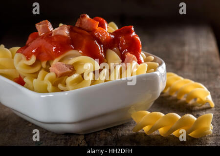 Les pâtes Fusilli à la tomate et bacon frit dans bol blanc sur fond de bois Banque D'Images