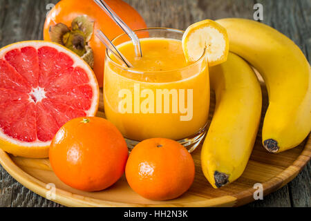 Fait frais smoothie à la banane jaune, pamplemousse, mandarine, kaki sur fond de bois Banque D'Images