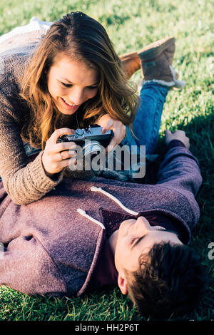 Jeune couple espiègle couchée sur l'herbe et de prise de vue avec un appareil photo, de jouissance et de relations concept Banque D'Images