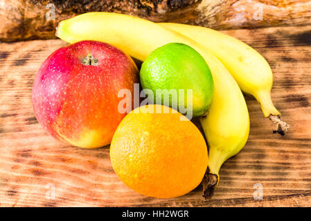 Produits frais et de fruits mûrs sur planche à découper en bois. Il y a une pomme, une orange sanguine, une lime et deux bananes sur le bord. Banque D'Images