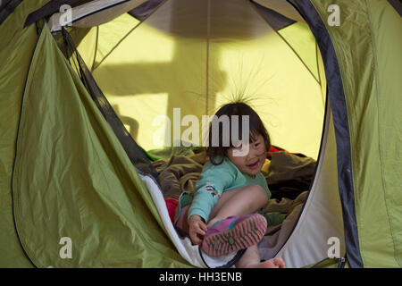 Une petite fille chinoise avec quelques cheveux en raison de l'électricité statique joue dans une tente pendant un voyage de camping familial en Chine. Banque D'Images