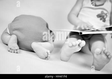 Petite fille est en train de lire un livre tog son bébé frère. Photo en noir et blanc avec soft focus sur leurs pieds. Les valeurs de la famille Banque D'Images