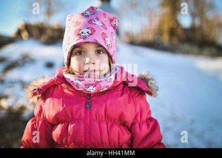 Little girl in winter clothes standing in Mountain Ski Resort. Un enfant avec chapeau, écharpe et manteau d'hiver est à la recherche à l'appareil photo à l'extérieur par temps neigeux nat Banque D'Images